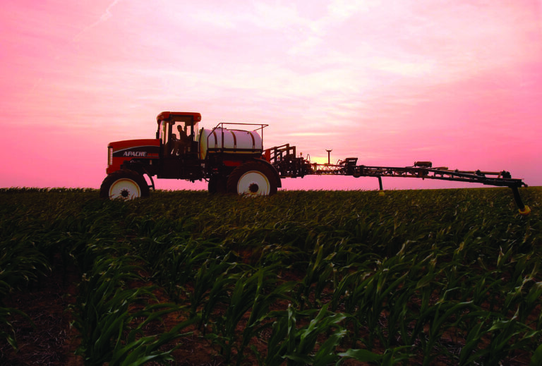 side of old apache sprayer with pink sunset behind it